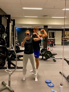 two people in a gym doing squats with their arms up and one person taking a selfie