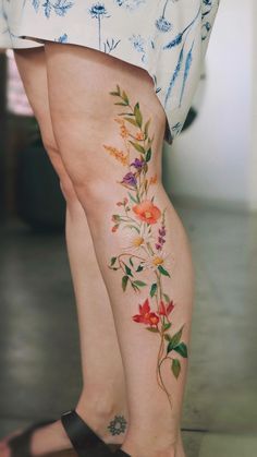 a woman's legs with tattoos on them and flowers painted on the side of her leg