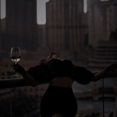 a woman standing on a balcony holding a wine glass in her hand and looking at the city