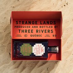 an orange box with two bottles in it sitting on the sand next to a bottle of liquor