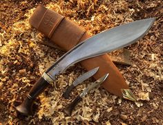 two knives are laying on the ground next to some wood shavings and a knife sheath