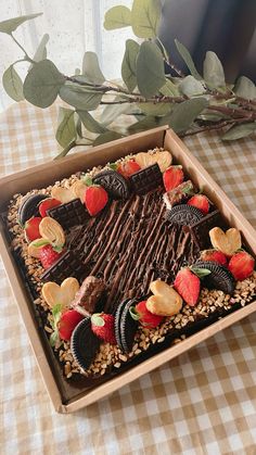 a chocolate cake in a box with strawberries and crackers on the top, sitting on a checkered tablecloth