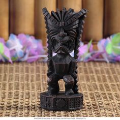 a carved wooden figurine sitting on top of a woven tablecloth next to flowers