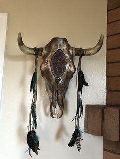 a bull's skull mounted on the wall with feathers hanging from its back end