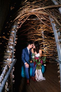 a bride and groom sitting on a bench in the middle of an arch made out of branches