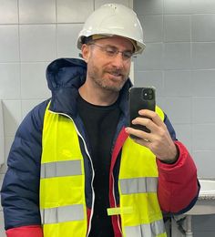 a man wearing a hard hat and reflective vest holding a cell phone