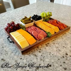 a wooden tray filled with different types of cheeses and fruit on top of a counter