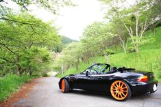 a black sports car with orange wheels parked on the side of a road next to trees