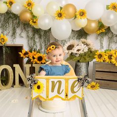 a baby is sitting in a cake box with sunflowers and balloons around it