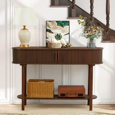 a wooden table sitting under a stair case next to a lamp and vase with flowers on it