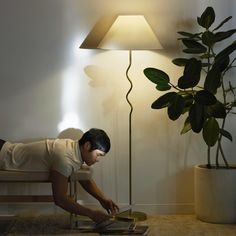 a man laying on the floor next to a lamp with a plant in front of him