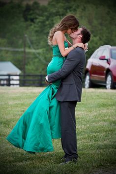 a man in a suit and woman in a green dress hugging each other on the grass