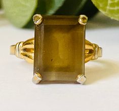 This vintage ring is a size 8.  It features a smokey brown rectangular stone set in an unmarked gold tone band. There is age related wear to the band. Please see pictures.  Please be aware that we are not jewelry experts. We have a sincere love of all things vintage especially vintage jewelry. We hope to share our finds with you. That being said, we describe our items to the very best of our ability. Please view all photos and know that each phone or computer screen may display slightly different colors. Please ask any and all questions. We gladly accept returns and provide shop credit or refund upon receiving the item back. The buyer pays return shipping unless the item is grossly damaged. In that case, please send us a photo of the damage. Please contact us immediately with any order or Bronze Gemstone Vintage Jewelry, Classic Brown Gemstone Rings, Artisan Brown Gemstone Rings, Brown Large Stone Ring, Brown Large Stone Ring Jewelry, Crystal Cluster Earrings, Brown Stone, Blue Stone Ring, Black Bead Necklace