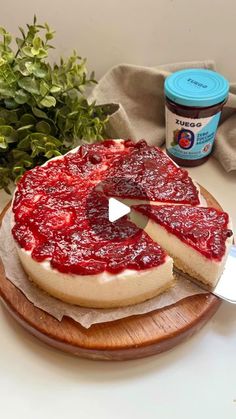 a cheesecake on a wooden plate with a piece missing from it and a jar of jam in the background