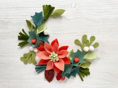 felt christmas wreath with poinsettis, holly and pine cones on white wooden background