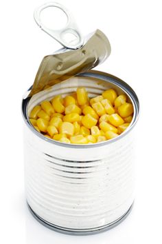 an open tin can filled with corn and scissors on top of white background, closeup