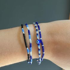 two bracelets with evil eyes are on someone's arm, one is blue and the other is white