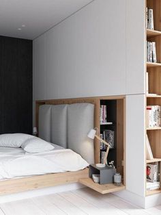 a bed with white sheets and pillows in a room next to a book shelf filled with books