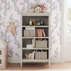 a book shelf with baskets and stuffed animals on it in front of a floral wallpaper