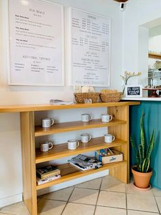 a coffee shop counter with cups on it next to a potted plant and menus