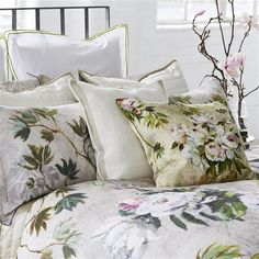 a bed covered in lots of pillows next to a vase with flowers on top of it