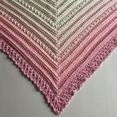 a pink and white crocheted blanket sitting on top of a gray tablecloth