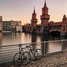 two bicycles parked next to each other on a bridge over water with buildings in the background