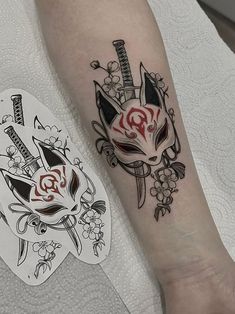 a tattoo on the arm of a person with a cat mask and flowers around it