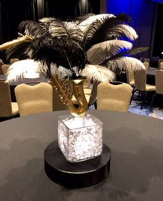 a table topped with a vase filled with feathers and a golden instrument on top of it