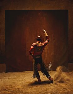 a man in a red jacket and hat kicking up dirt while wearing a cowboy hat