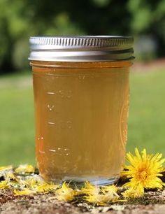 a jar filled with liquid sitting on top of a wooden table next to a flower