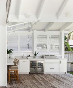 an outdoor kitchen with wooden floors and white walls, has shutters on the windows