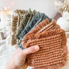 a hand is holding several pieces of woven material in front of a white vase with candles