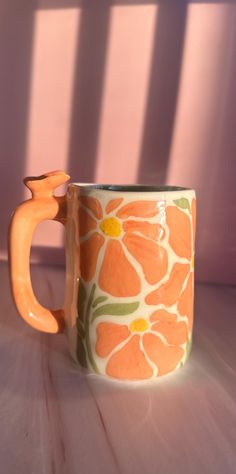 an orange and white flowered mug sitting on a table next to a pink wall