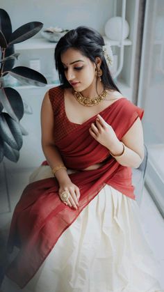 a woman in a red and white sari sitting on a window sill next to a potted plant