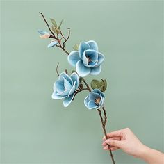 a hand is holding a fake flower on a twig with blue flowers in it