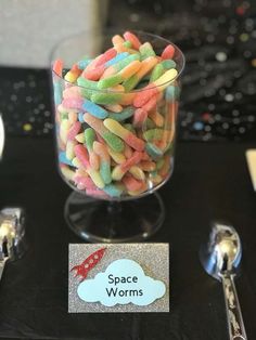 there is a glass bowl with candy in it on the table next to spoons and utensils