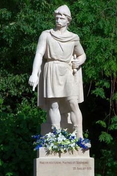 a statue of a man with flowers in his hand and trees in the back ground