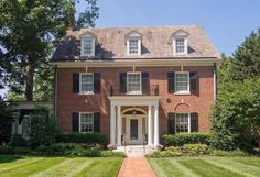 a large brick house with white trim and black shutters on the front door is surrounded by lush green grass