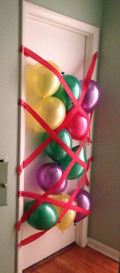 balloons tied to a wall in front of a door with red ribbon on it and some green, purple, yellow and pink balloons