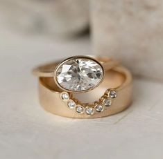 two gold wedding rings with an oval cut diamond in the center and small diamonds on each band