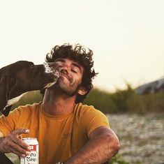 a man sitting on the ground next to a dog drinking out of a beer can