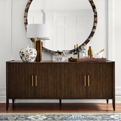 a large round mirror on top of a wooden dresser next to a lamp and vase