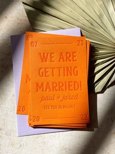 we are getting married cards on top of each other next to an orange paper fan