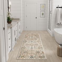 a bathroom with white walls and wood flooring has a large rug on the floor