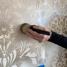 a person using a brush to paint a wall with floral designs on the wallpaper