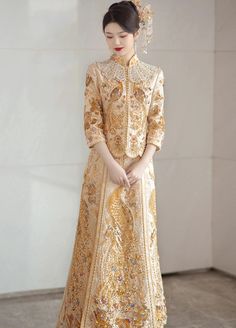 Color: gold Silhouette: A-line Length: long Neckline: mandarin collar Sleeves: three-quarter Fabric: satin Material: polyester Details: sequin embroidery, peacock embellishment A gold Chinese wedding dress for women Captivate everyone by your presence in a gold Chinese wedding dress at the ceremony. Exude elegance and style in this stunning bridal gown made in a luxurious golden shade and decorated with exquisite embroidery. Timeless and chic, this Chinese wedding dress has a charming style and graceful details. Celebrate your culture in this refined wedding ensemble that is inspired by traditional Qun Kwa. It includes a tailored two-piece set that combines a fitted jacket and a feminine A-line skirt. This gold wedding gown is a fantastic option to wear for a tea ceremony as it embodies th Peacock Embellishment, Gold Qipao, Gold Cheongsam, Chinese Bridal Dress, Gold Wedding Gown, Chinese Style Wedding Dress, Modern Chinese Wedding Dress, Qipao Wedding Dress, Cheongsam Wedding Dress