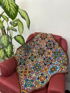 a red chair with a colorful blanket on it next to a potted green plant