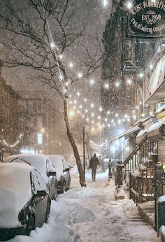 a city street covered in snow at night with people walking on the sidewalk and parked cars