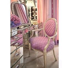 a pink chair sitting in front of a mirror next to a dresser with flowers on it